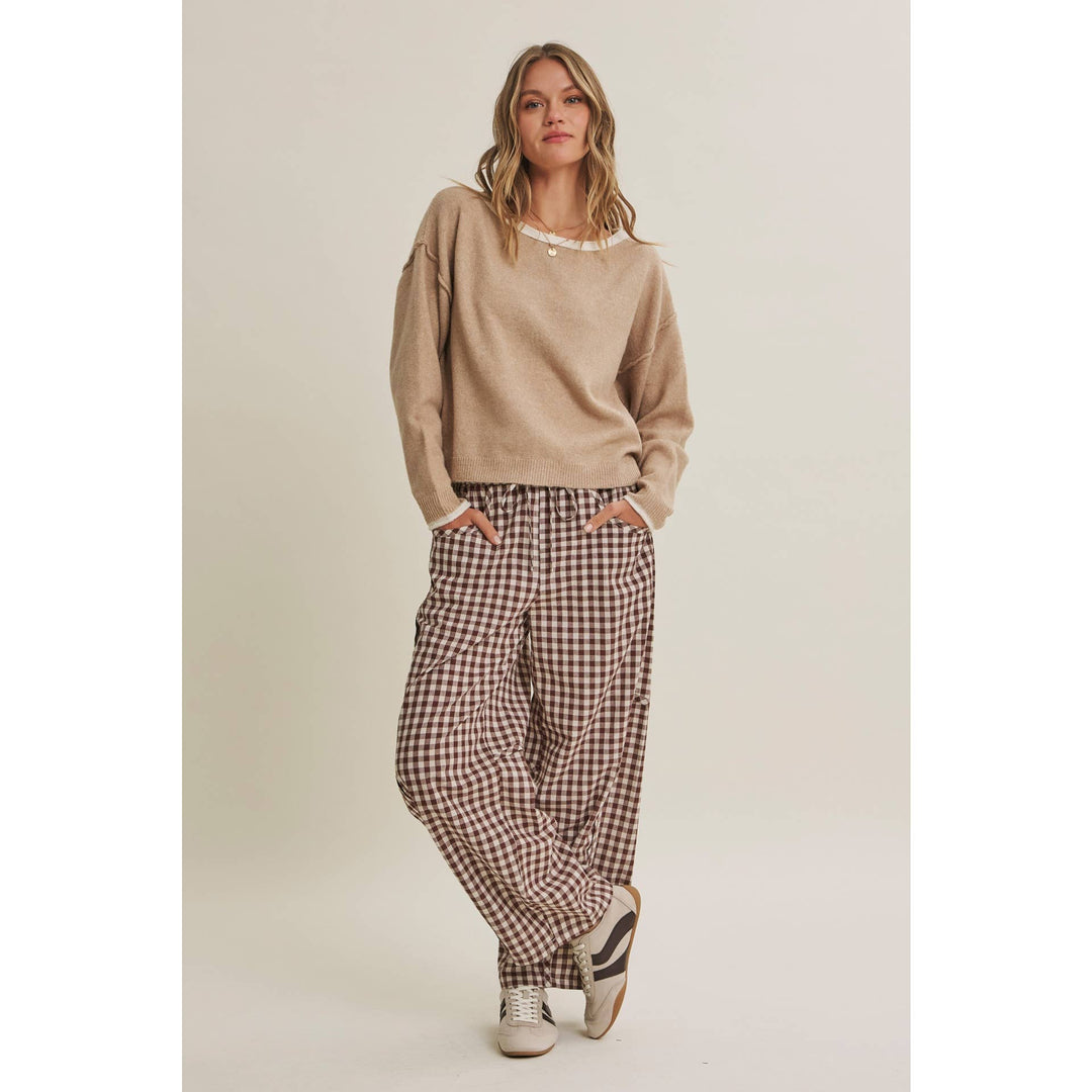 Woman wearing a beige sweater and checkered pants on a plain background