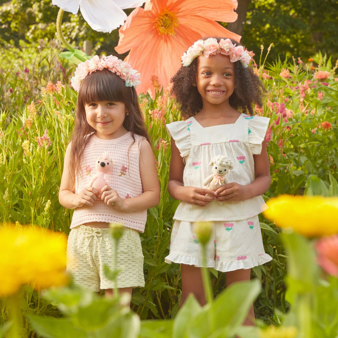 Two young girls standing in a field of flowers, holding knitted plush animals.