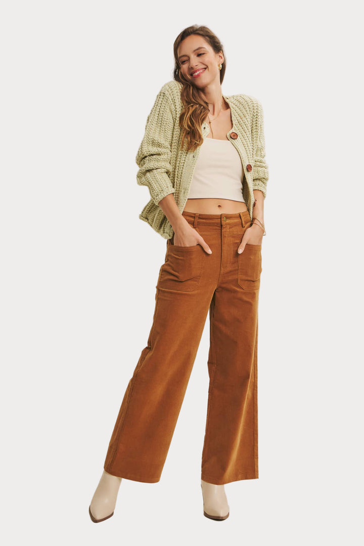 Woman wearing a green cardigan, white top, and brown pants on a beige background