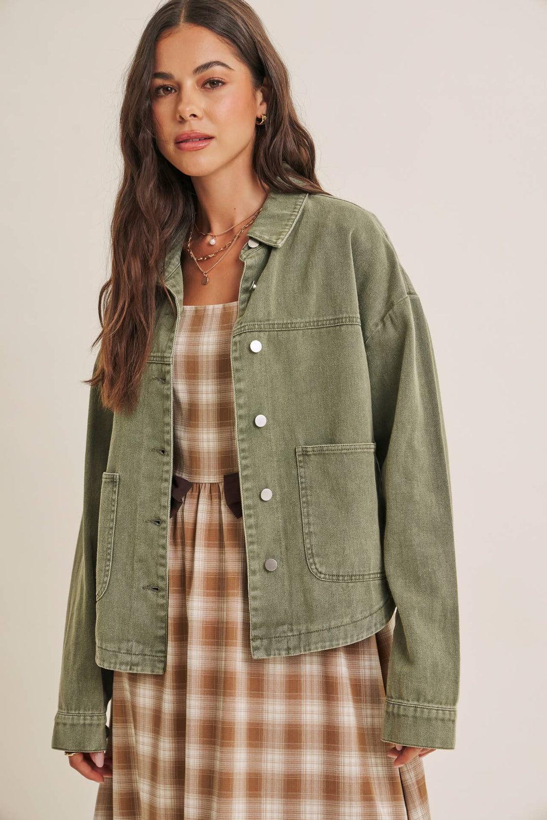 Woman wearing a olive green jacket over a plaid dress on a beige background