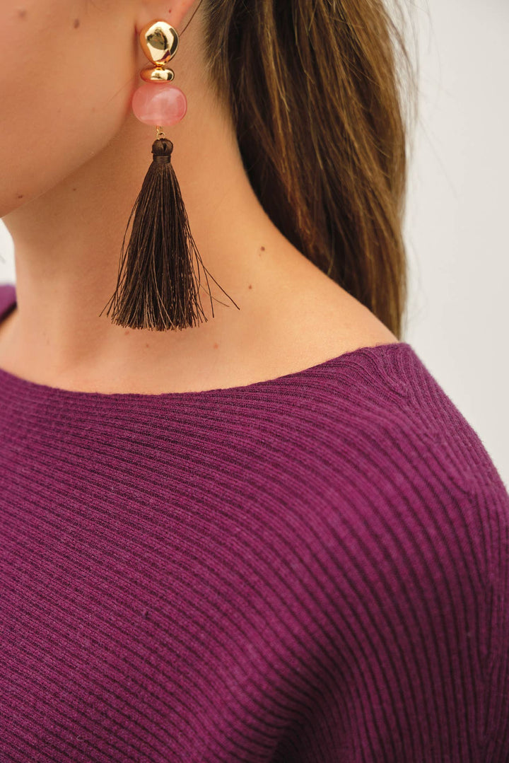 Close-up of a tassel earring on a person wearing a purple sweater.