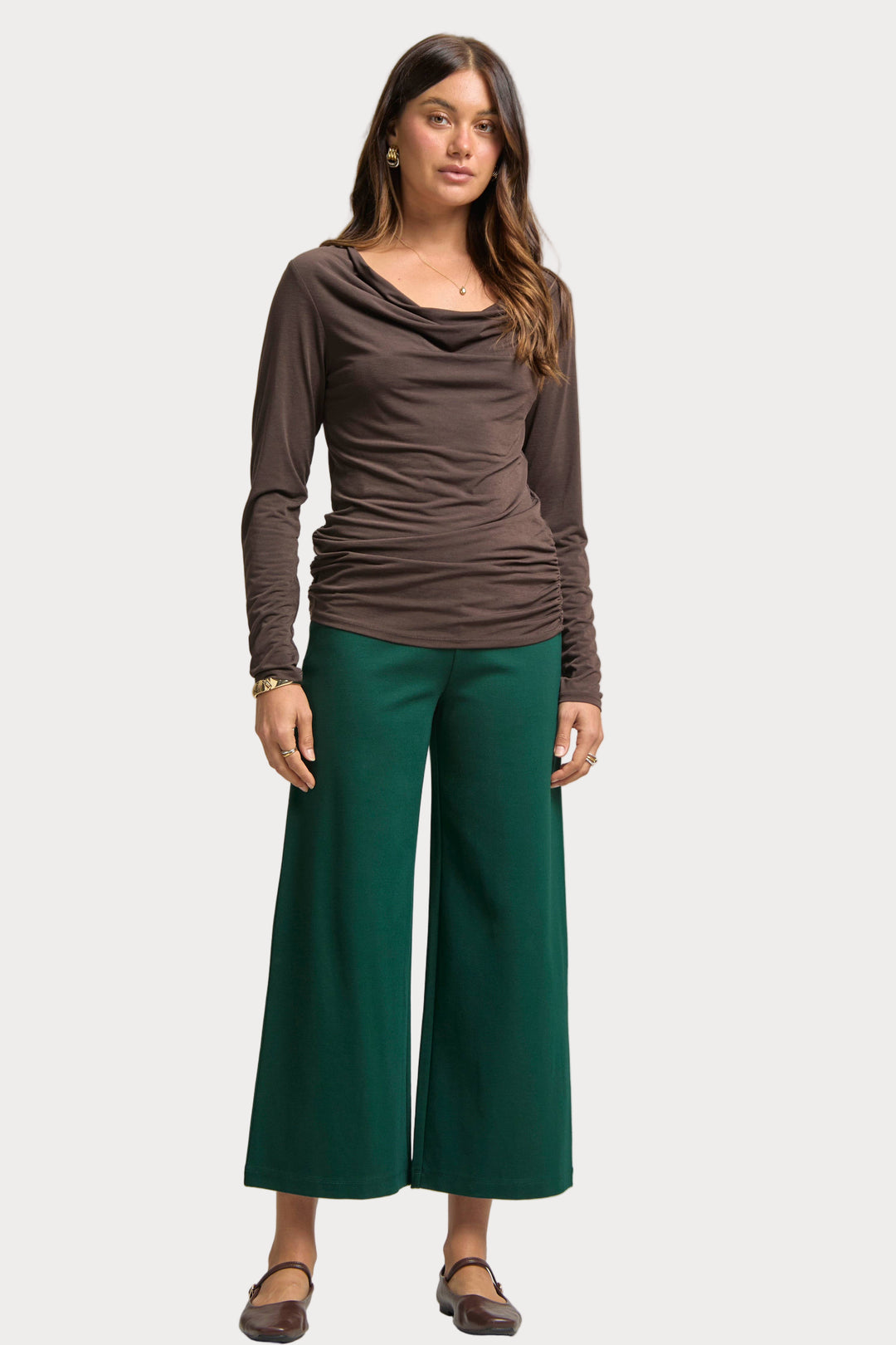 Woman wearing a brown long-sleeve top and green wide-leg pants on a plain background