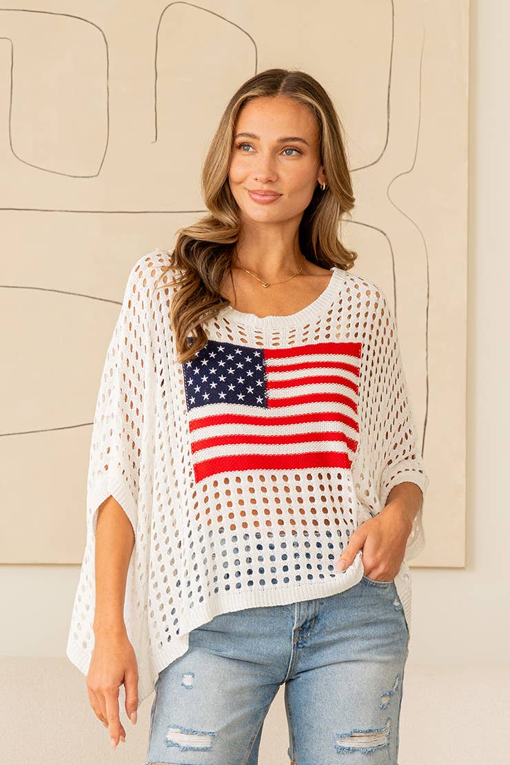 Woman wearing white open-knit sweater top with American flag design and denim jeans
