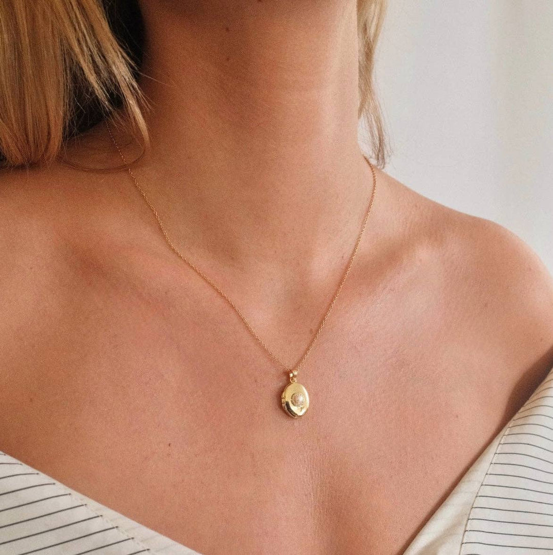 Gold necklace with a pendant on a person wearing a striped shirt.