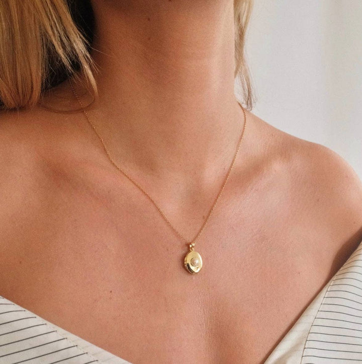 Gold necklace with a pendant on a person wearing a striped shirt.