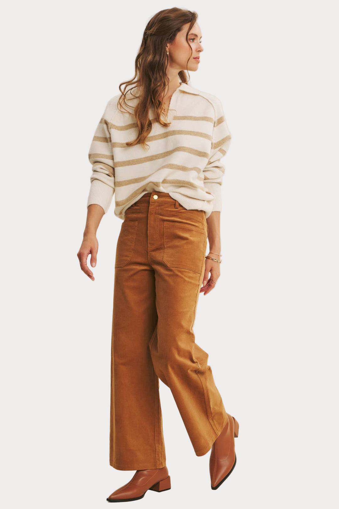 Woman wearing a striped sweater and brown pants against a plain background