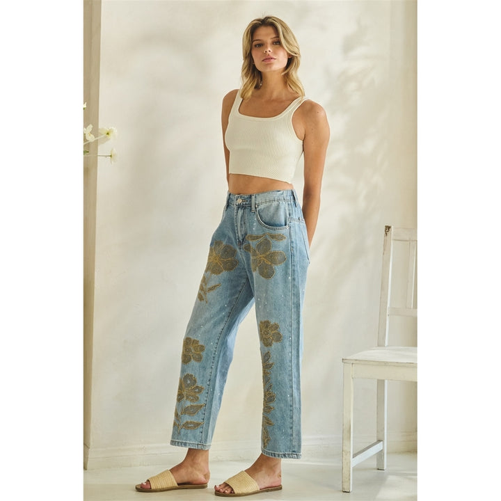 Woman wearing a white tank top and floral jeans in a room with a white door and chair.