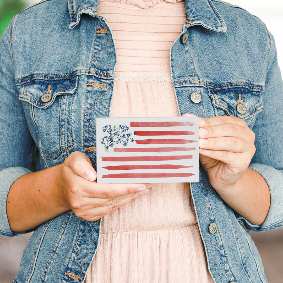 Person holding a block sign with a watercolor American flag design.
