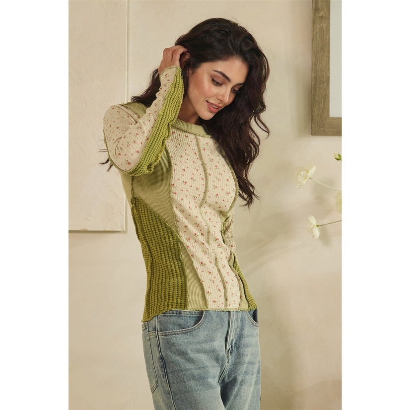 Woman wearing a green and beige patterned top with blue jeans indoors.