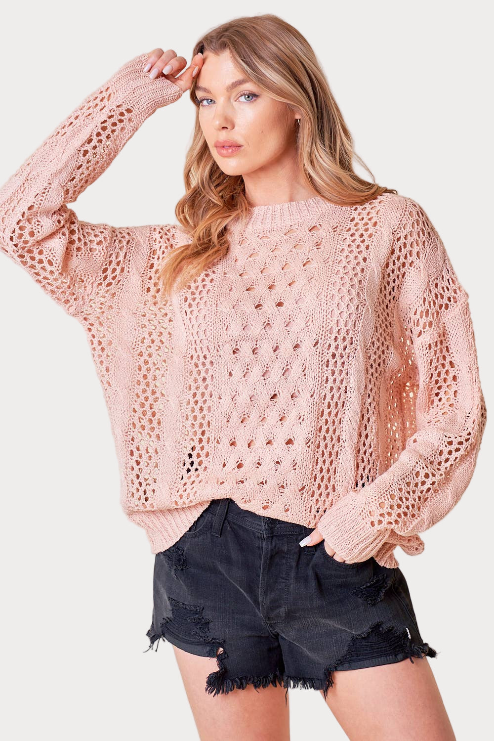 Woman wearing a pink crochet sweater and black shorts on a white background