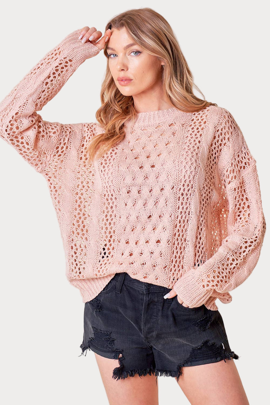Woman wearing a pink crochet sweater and black shorts on a white background
