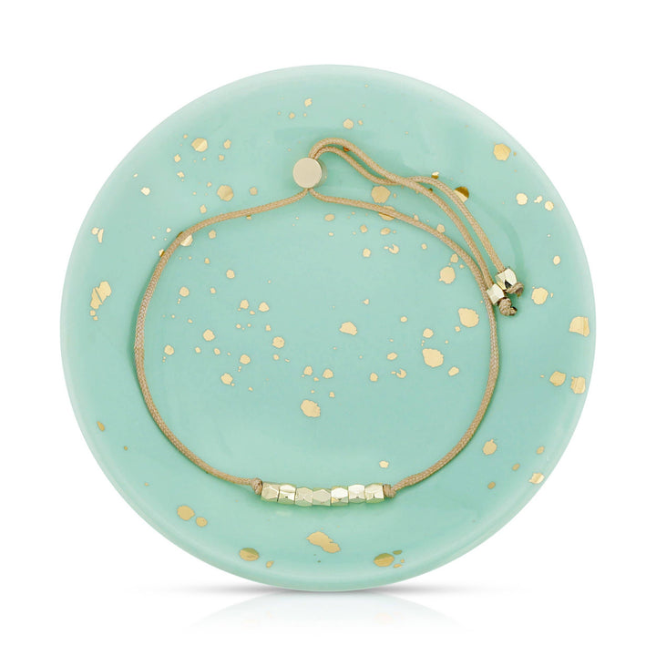 Gold bead & cord bracelet on a round turquoise dish with gold speckles