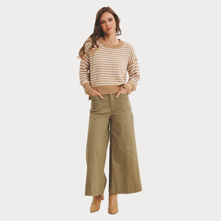 Woman wearing a checkered sweater and wide-leg pants on a plain background