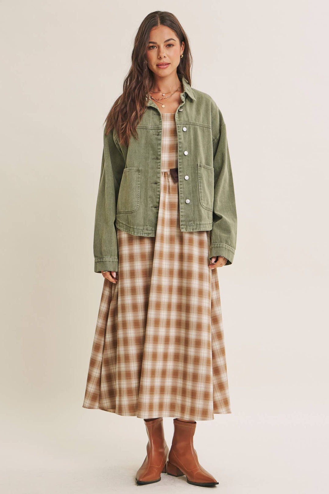 Woman wearing a olive green jacket over a plaid dress on a beige background