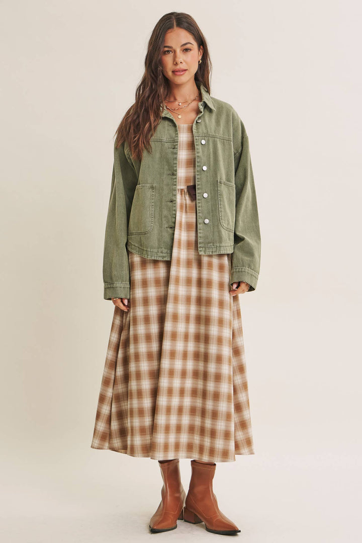 Woman wearing a olive green jacket over a plaid dress on a beige background