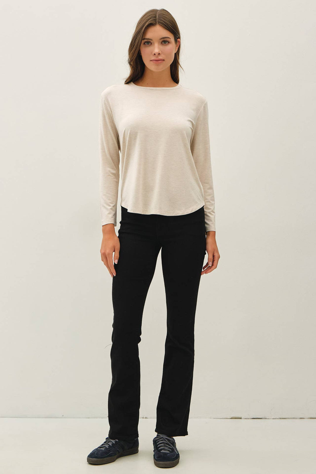 A woman modeling a cream long-sleeve knit top and black pants against a plain light gray studio background.
