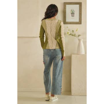 Woman wearing a green sweater and blue jeans standing in a room with a vase and plant.