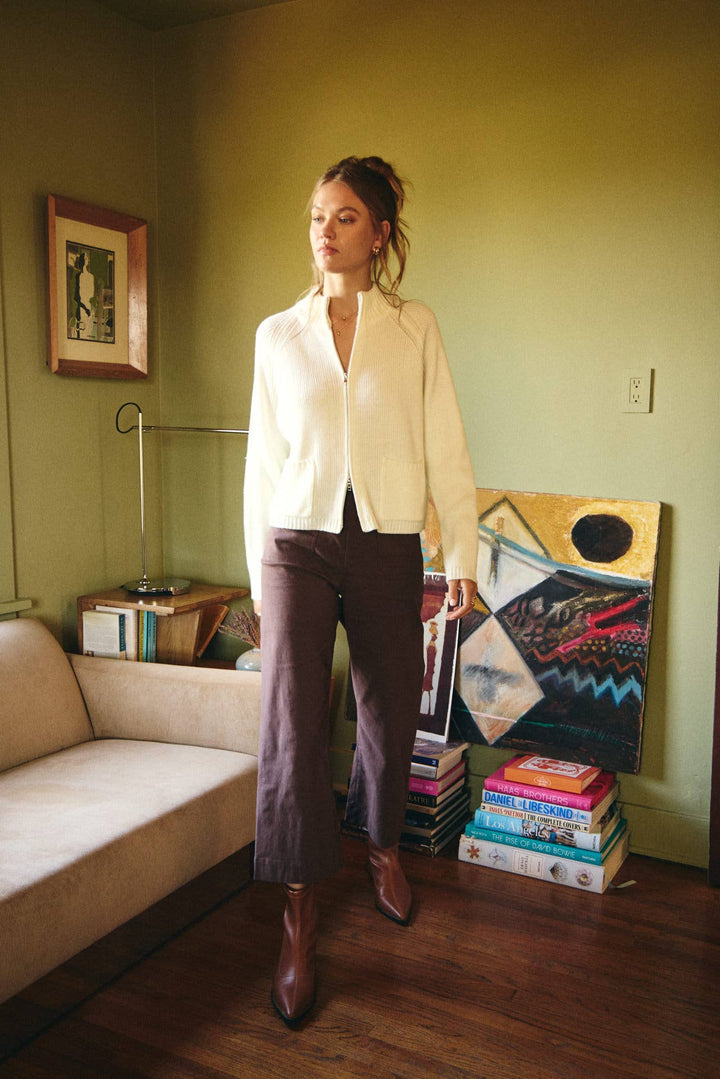 Woman standing in a living room with books and a painting on the wall.