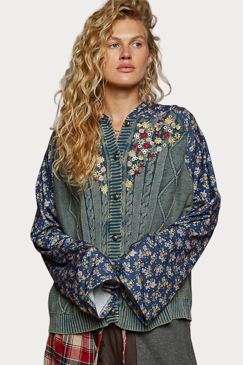 Woman wearing a hooded sweater with floral embroidery and patterned knit sleeves, styled in a relaxed boho look.