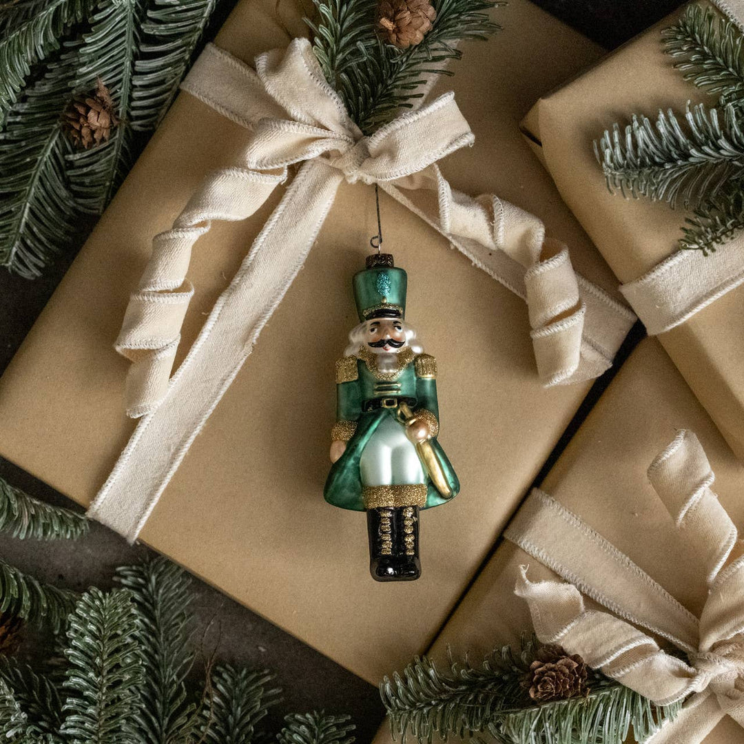 glass teal nutcracker ornament with gold accents displayed on wrapped gifts