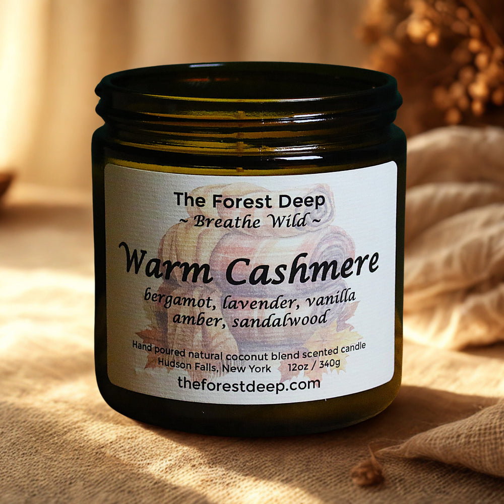 Candle jar labeled 'Warm Cashmere' by 'The Forest Deep' on a soft surface.