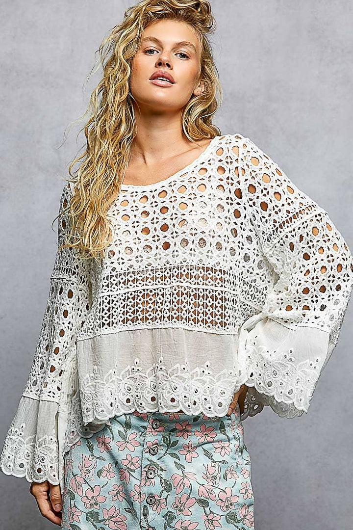Model wearing The Briar Rose Crochet Blouse featuring intricate open crochet, embroidered eyelet cotton panels, long bell sleeves, and a relaxed bohemian silhouette in ivory.