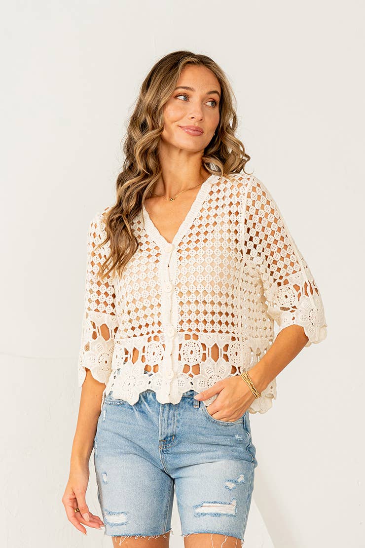 Woman wearing cream crochet button-down top with scalloped lace hem and distressed denim shorts