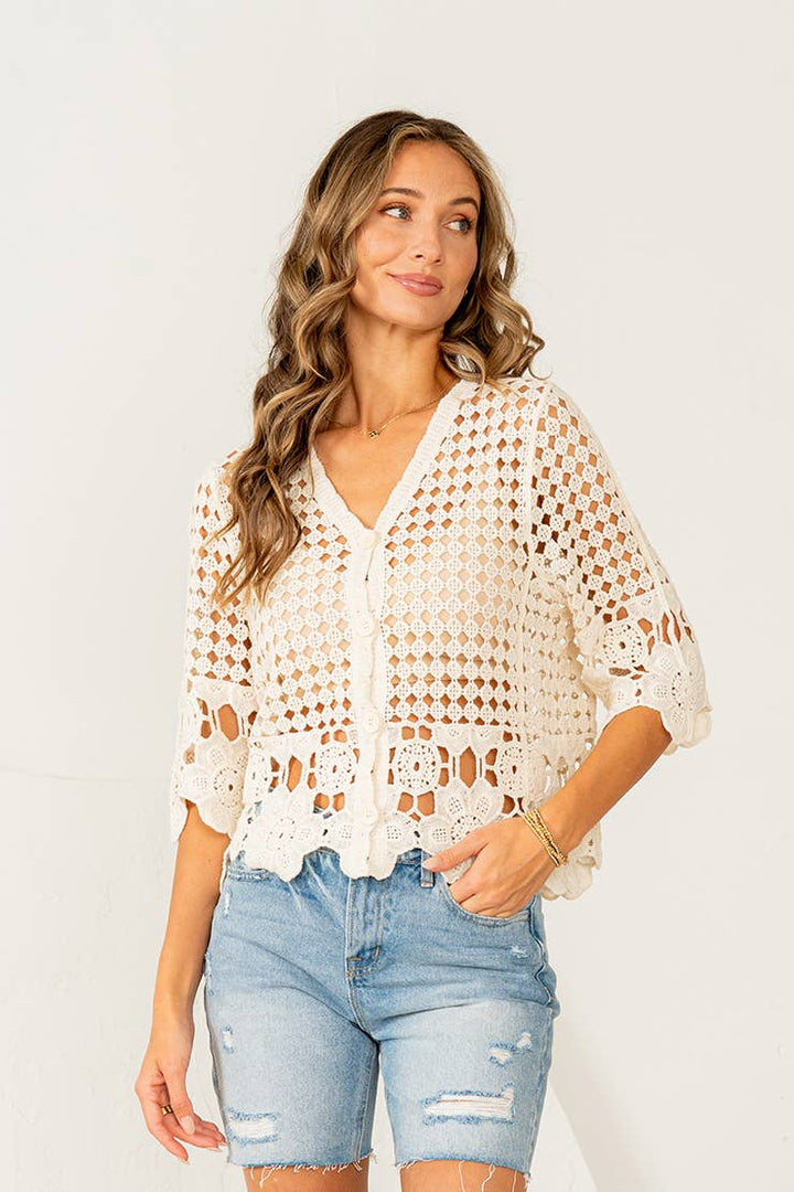 Woman wearing cream crochet button-down top with scalloped lace hem and distressed denim shorts
