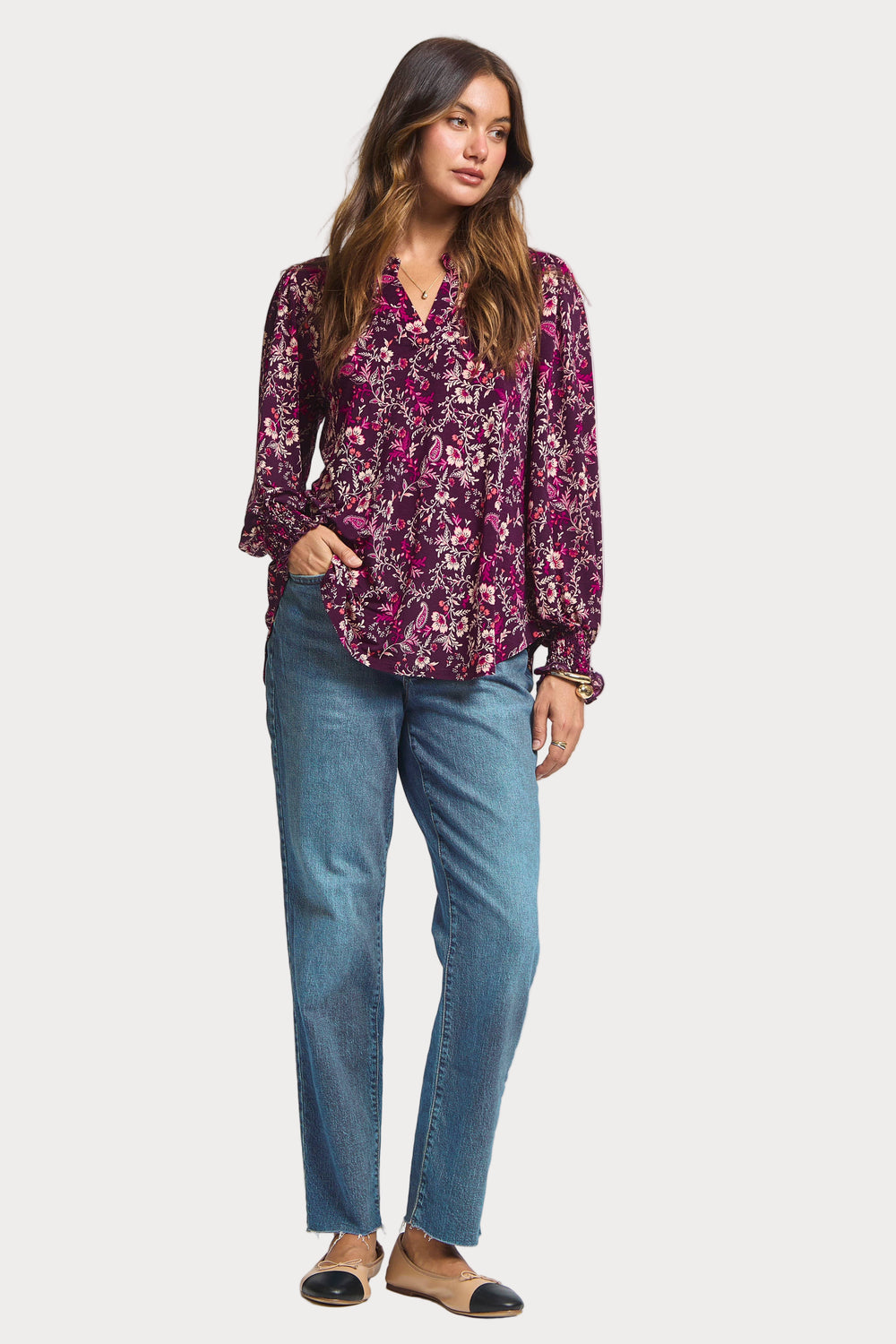 Woman wearing a purple floral blouse and blue jeans on a white background