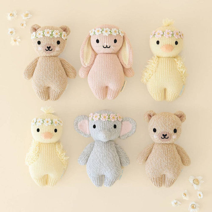 Set of six knitted toys in various colors with flower crowns on a beige background