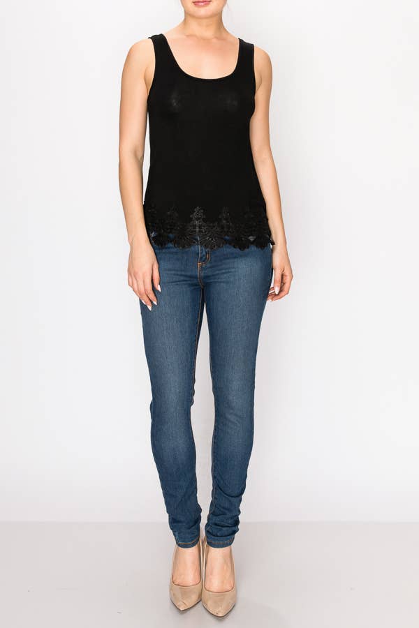 A model is shown from the torso up wearing a black scoop-neck tank top. The bottom hem is detailed with a delicate, scalloped black lace trim. She is wearing it with medium-wash blue jeans.

