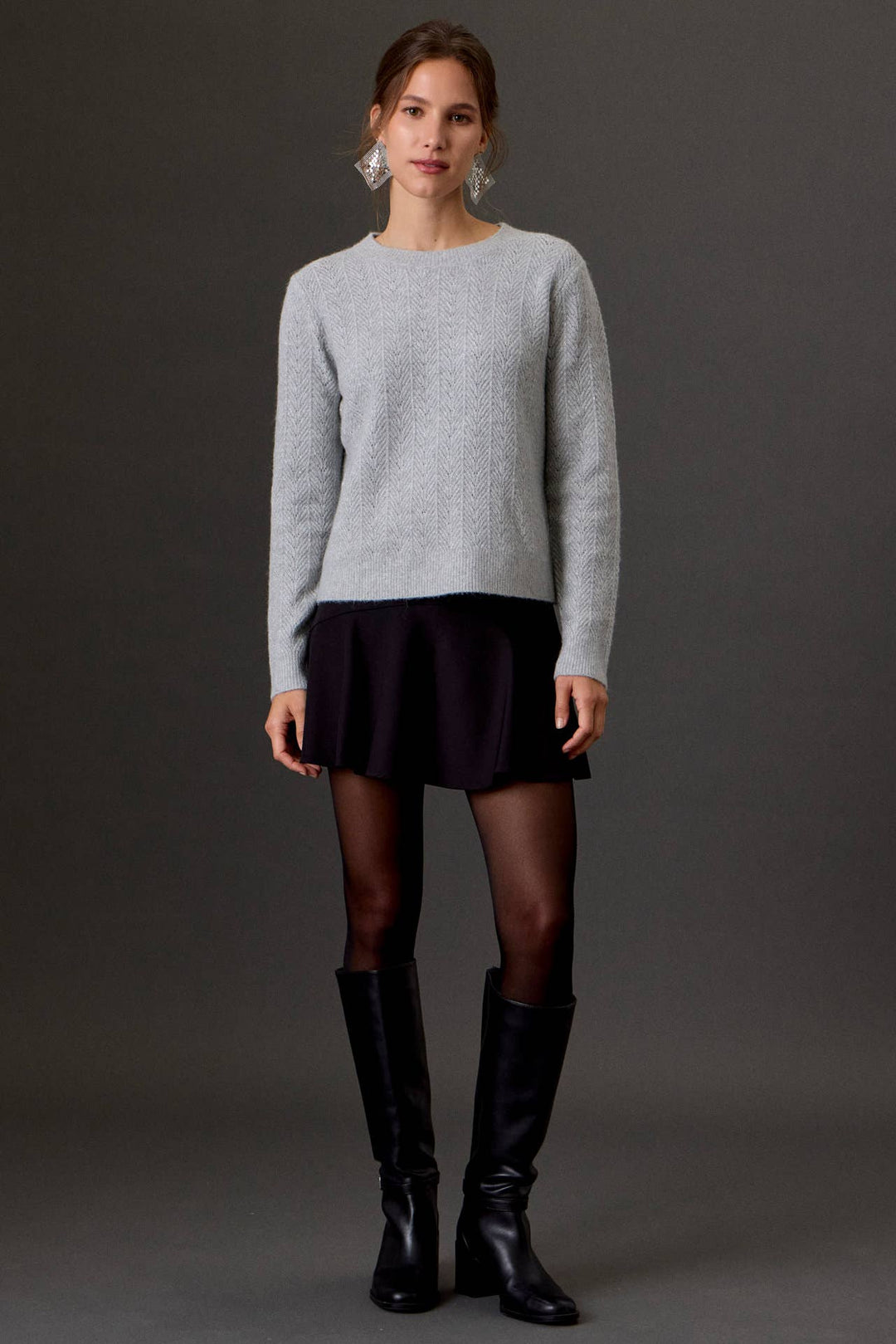 Be Cool Shimmering Moments light gray glitter pointelle knit sweater with crew neck, long sleeves, and relaxed cropped fit. Worn with black skirt, tights  & boots.