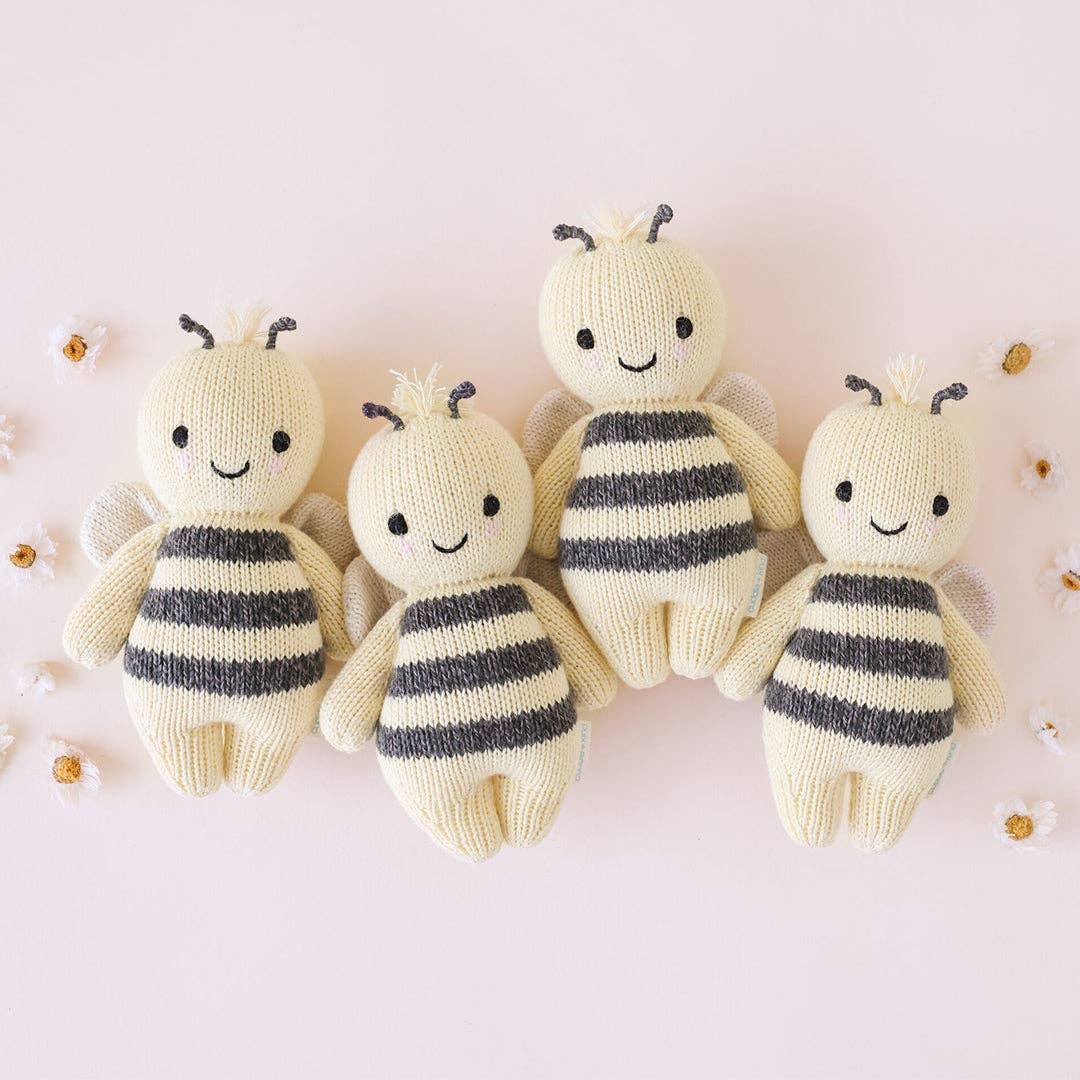 Four knitted bee toys with striped bodies on a light pink background