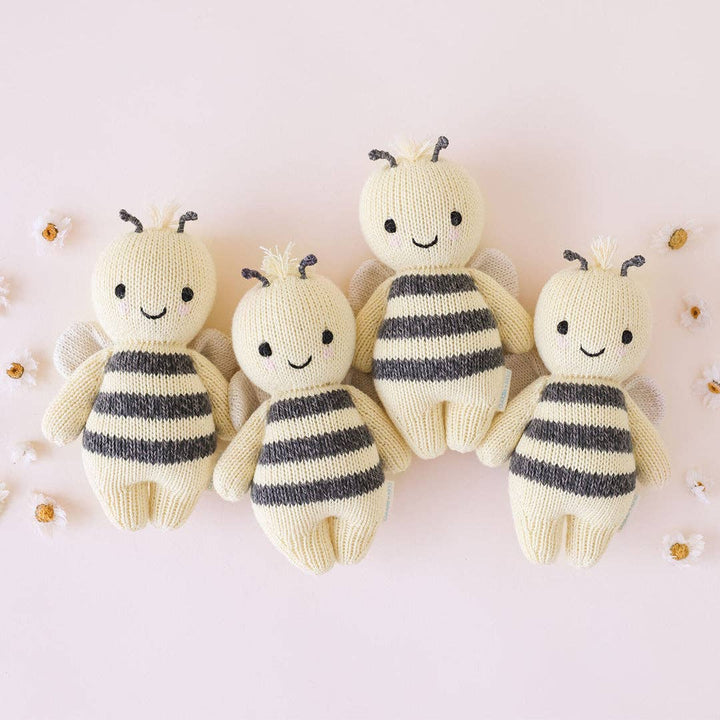 Four knitted bee toys with striped bodies on a light pink background