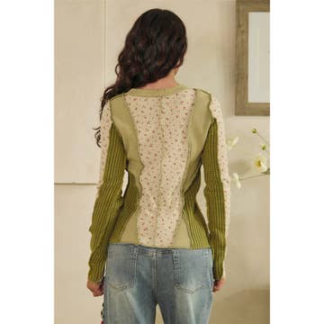 Woman wearing a green sweater with floral pattern on the back, standing in a room.