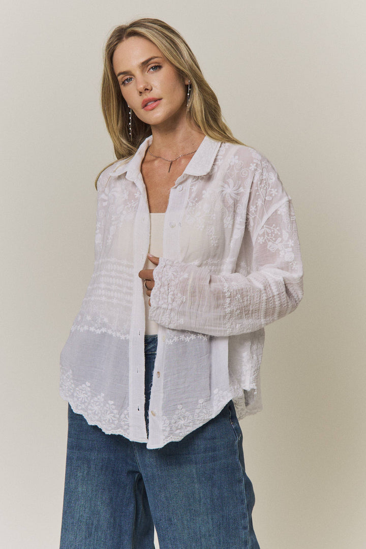 Woman wearing a light-colored lace embroidered blouse and blue jeans against a plain background