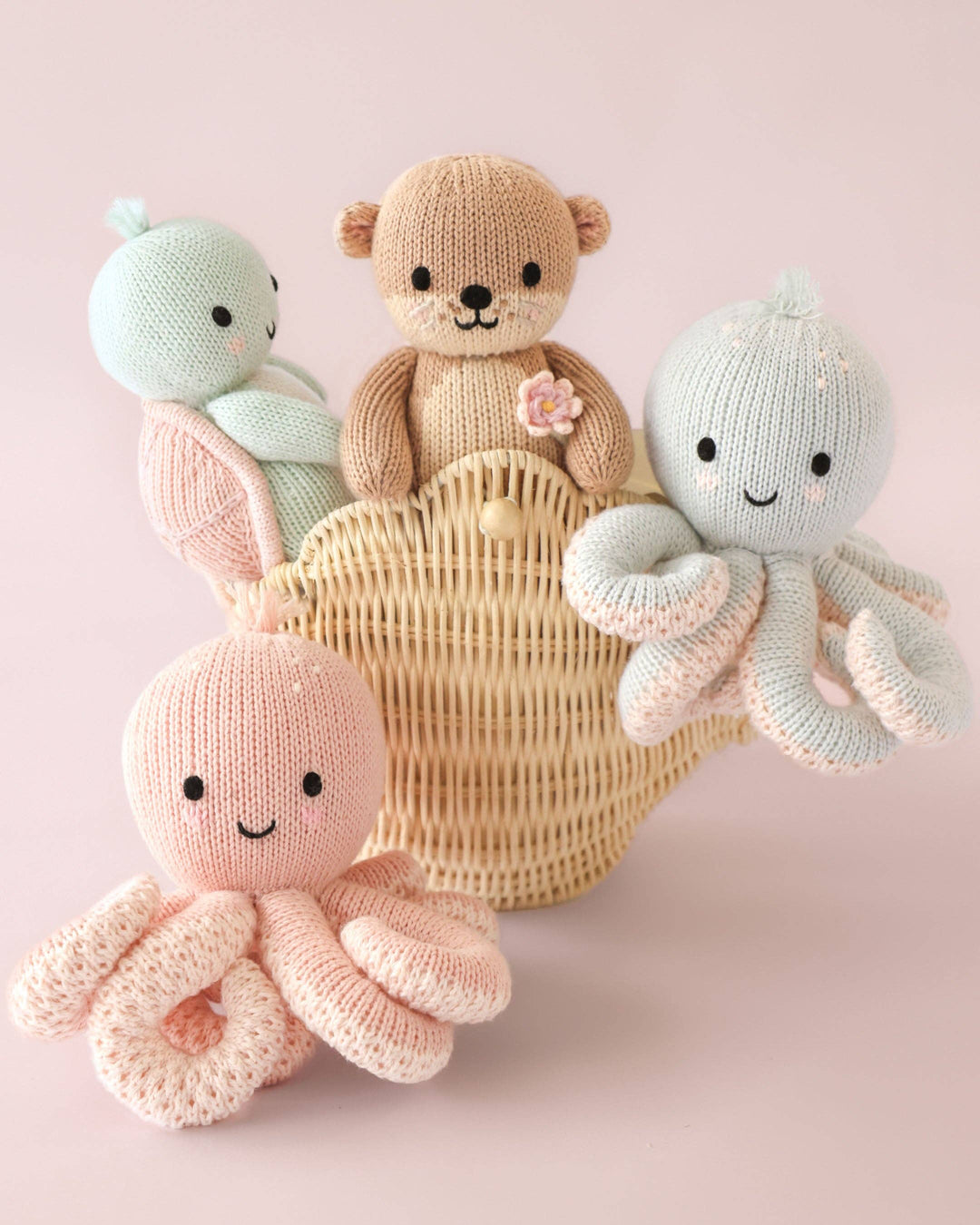 Knitted toys including a otter, octopus, and turtle in a basket on a pink background