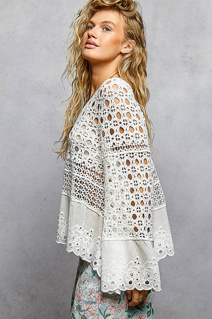 Model wearing The Briar Rose Crochet Blouse featuring intricate open crochet, embroidered eyelet cotton panels, long bell sleeves, and a relaxed bohemian silhouette in ivory.