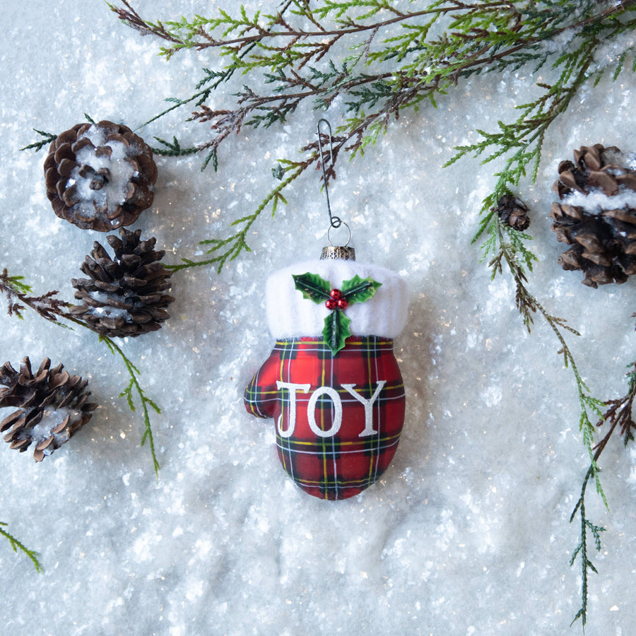 glass plaid mitten ornament with JOY lettering and holly detail on snowy background
