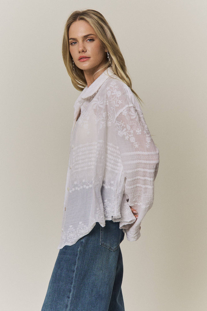 Woman wearing a light-colored lace embroidered blouse and blue jeans against a plain background