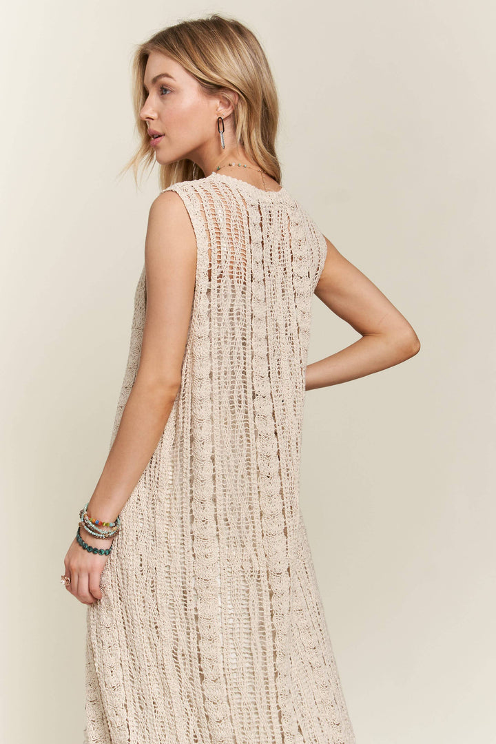 Woman wearing long beige crochet duster vest over a white floral dress