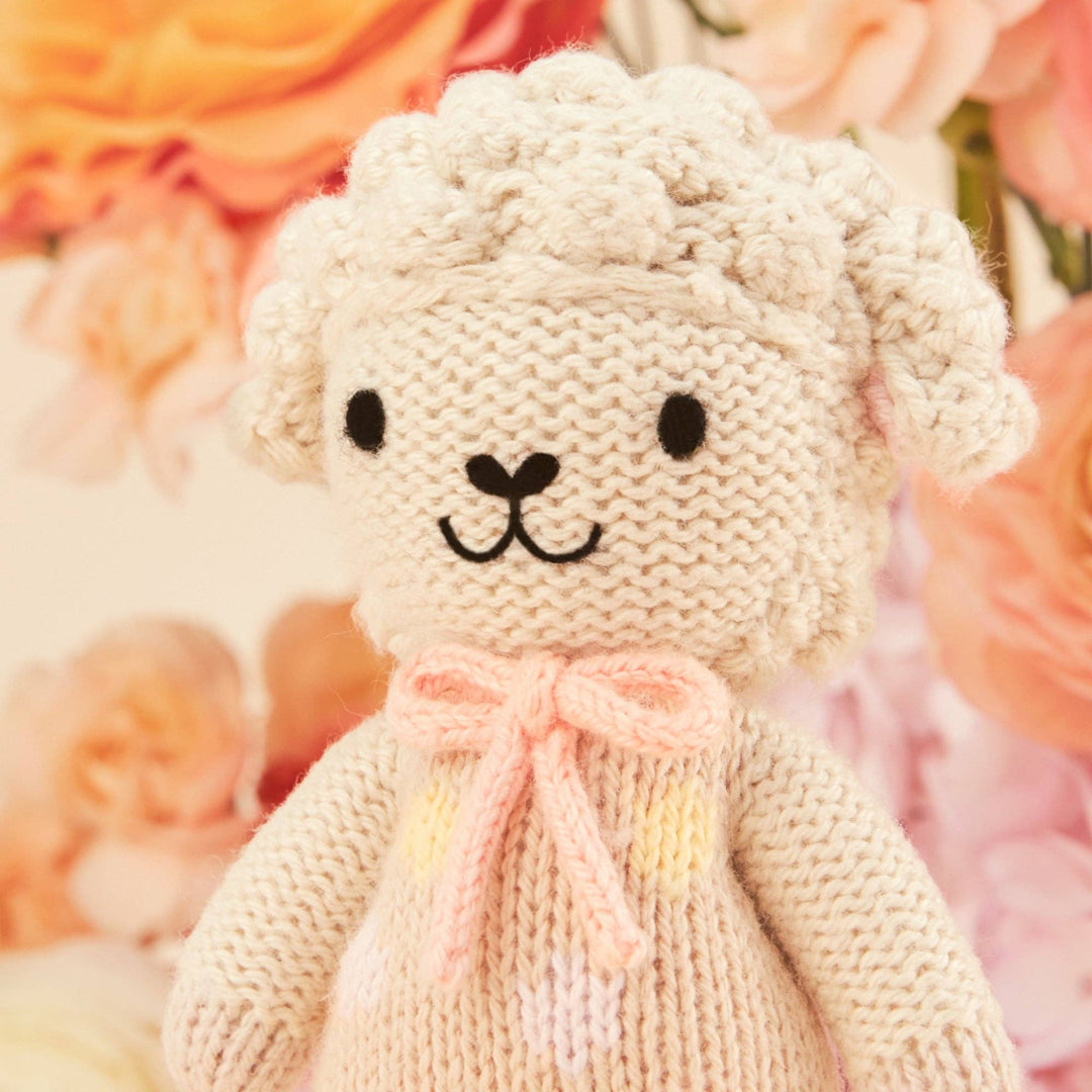 Knitted toy lamb with a pink bow on a floral background