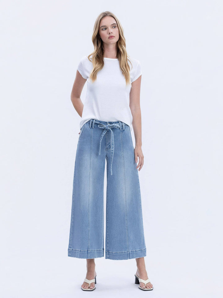 Woman wearing a white t-shirt and blue denim wide-leg pants on a white background