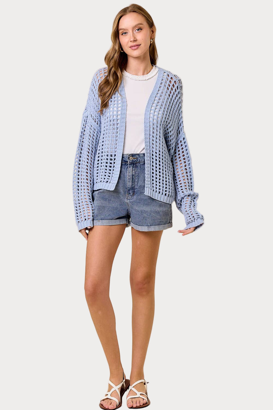 Woman wearing a light blue cardigan over a white shirt and denim shorts on a white background