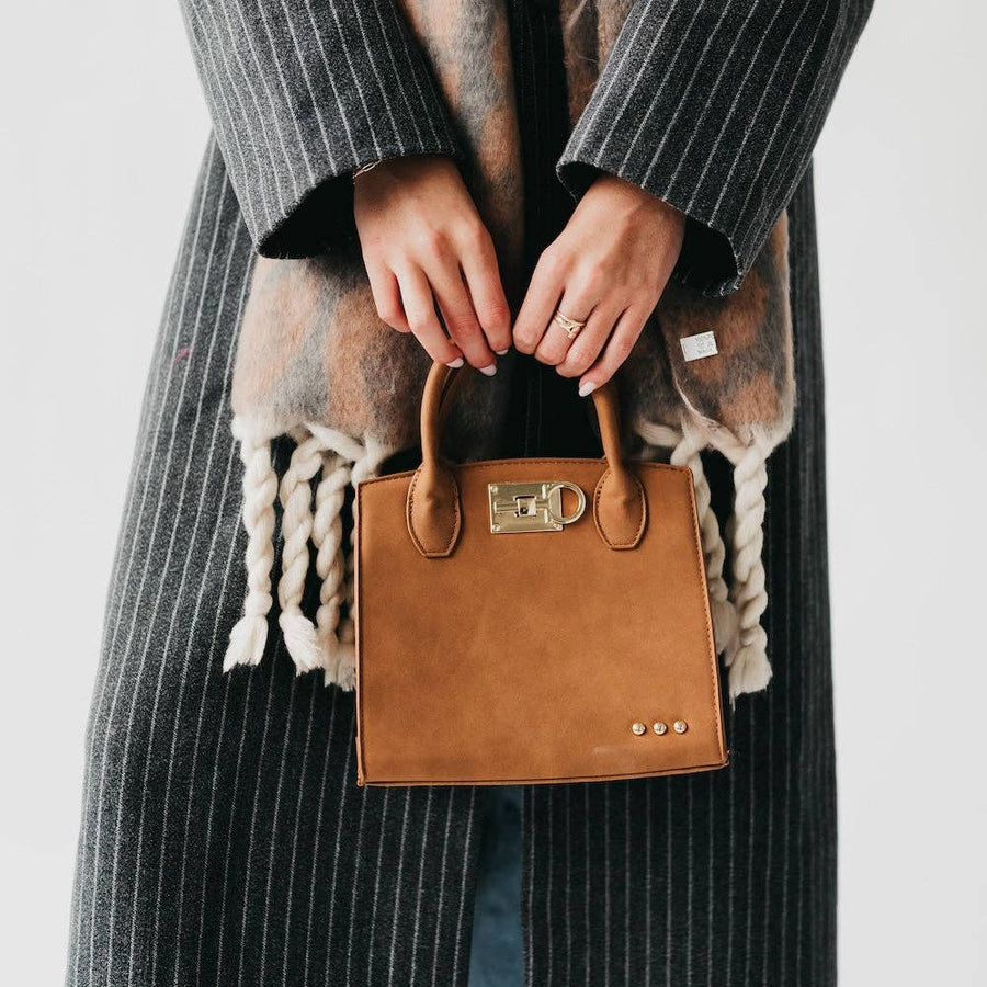 Model holding a small camel nubuck vegan leather tote with gold hardware.