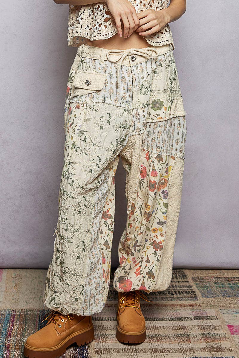 Model wearing The Cottage Bloom Patchwork Joggers by POL featuring vintage-inspired floral patchwork, textured jacquard details, oversized utility pockets, and a relaxed bohemian silhouette.