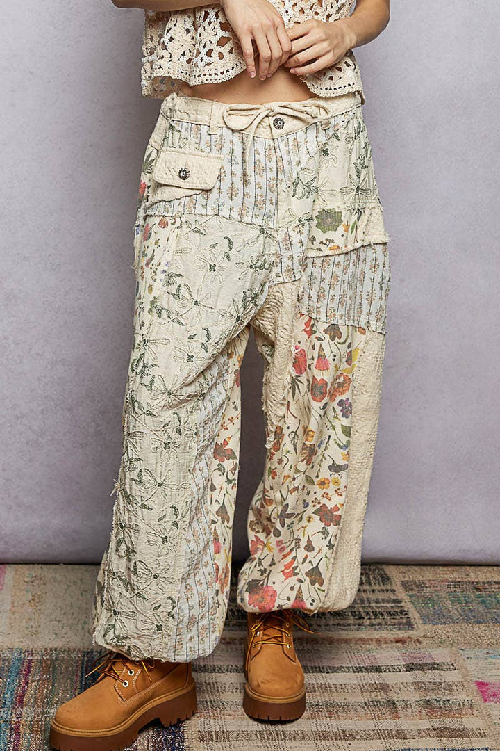 Model wearing The Cottage Bloom Patchwork Joggers by POL featuring vintage-inspired floral patchwork, textured jacquard details, oversized utility pockets, and a relaxed bohemian silhouette.