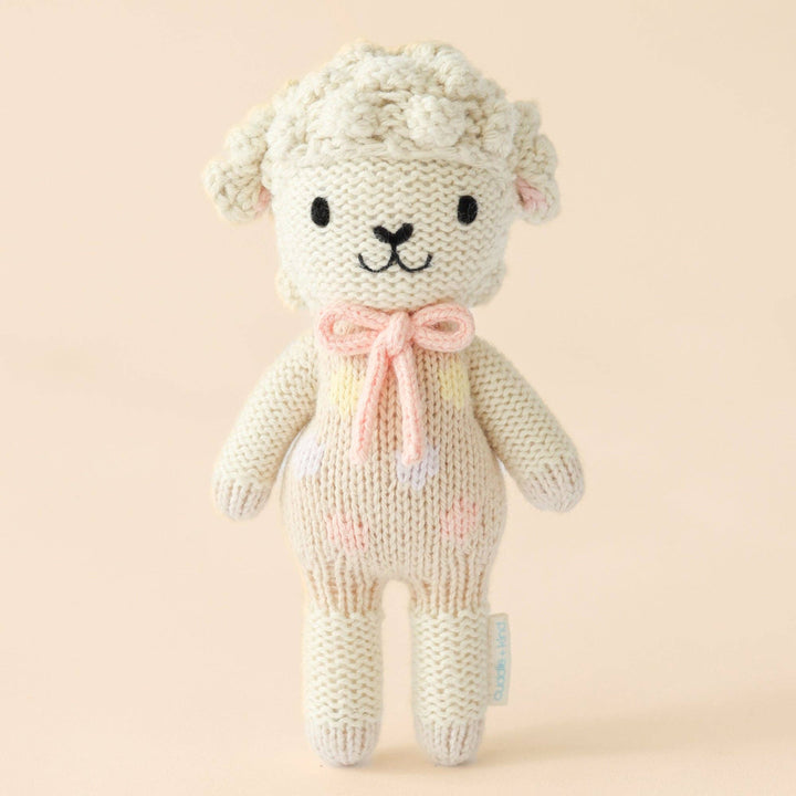 Knitted toy lamb with a pink bow on a beige background
