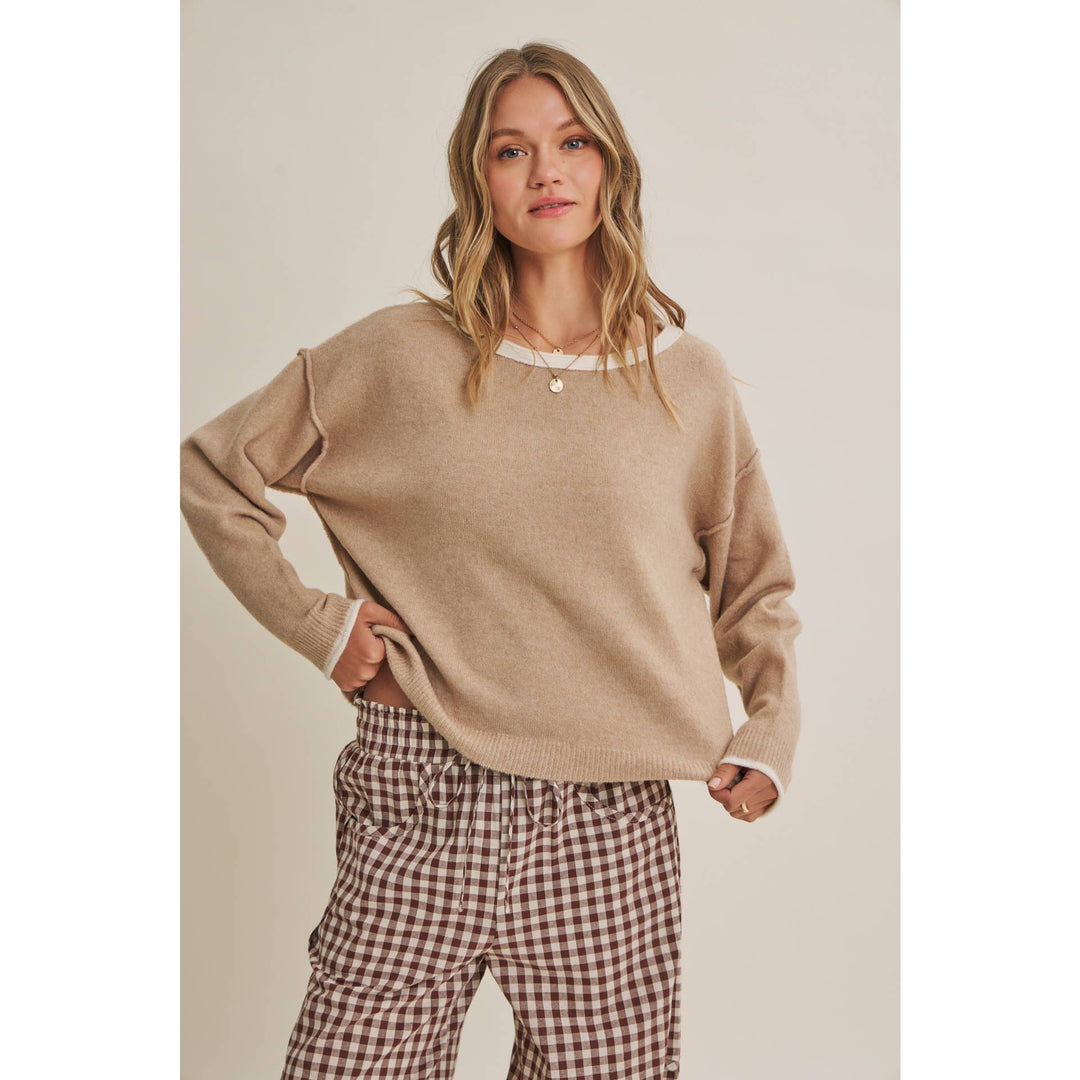 Woman wearing a beige sweater and checkered pants against a plain background