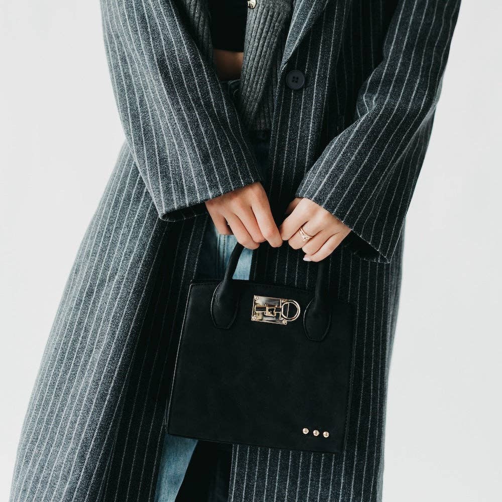 Person wearing a long pinstripe coat holding a black handbag with a gold clasp on a light gray background